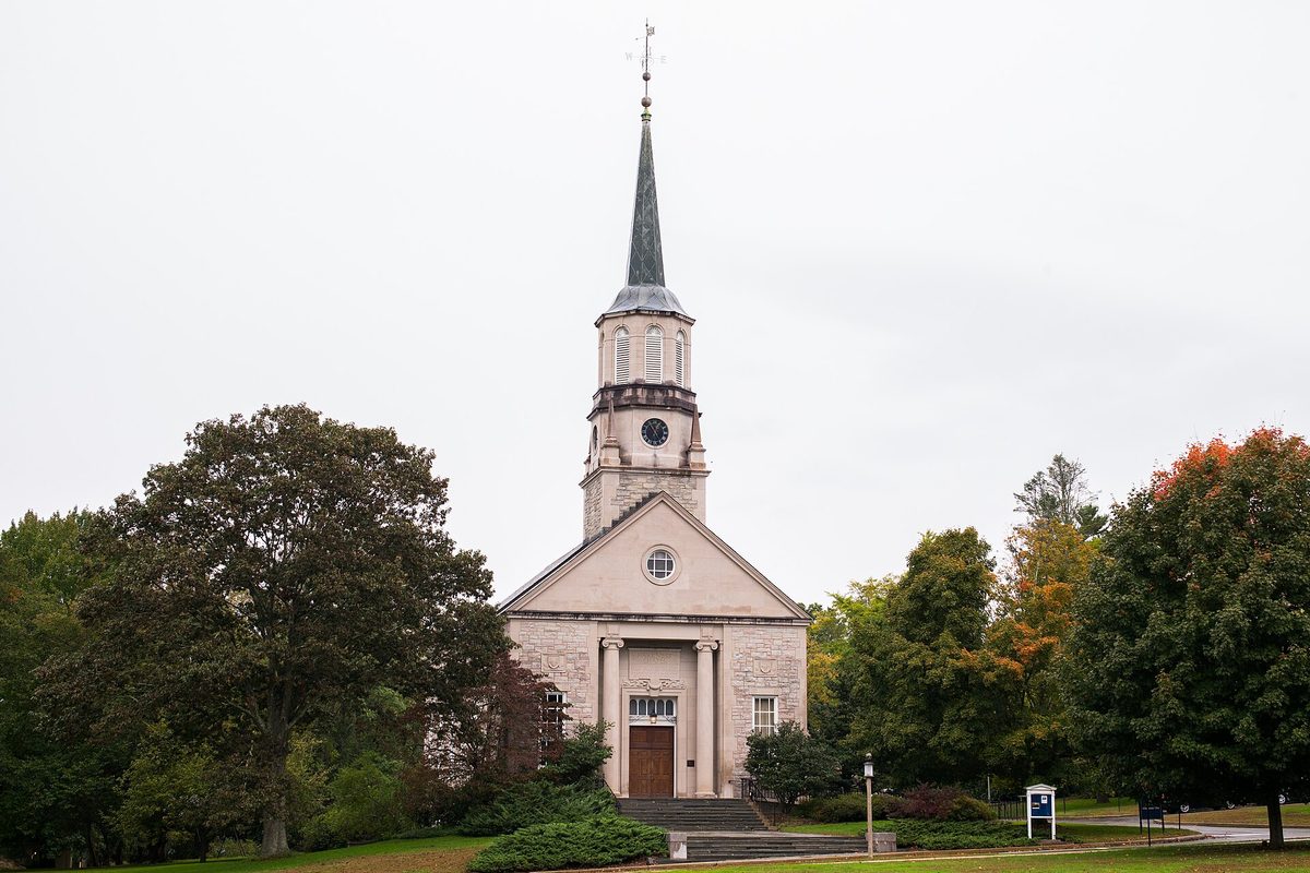Harkness Chapel at Connecticut College in New London, a stone chapel with a columned entrance and a tall steeple, framed by trees on an overcast day