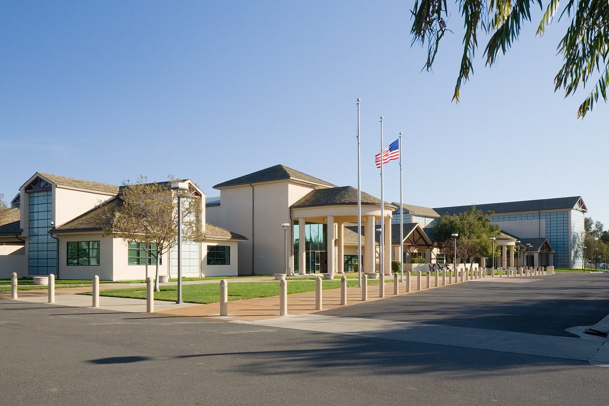 The Silliman Activity and Family Aquatic Center in Newark, a tan building with a columned entrance, flagpoles and a wide plaza under a clear blue sky