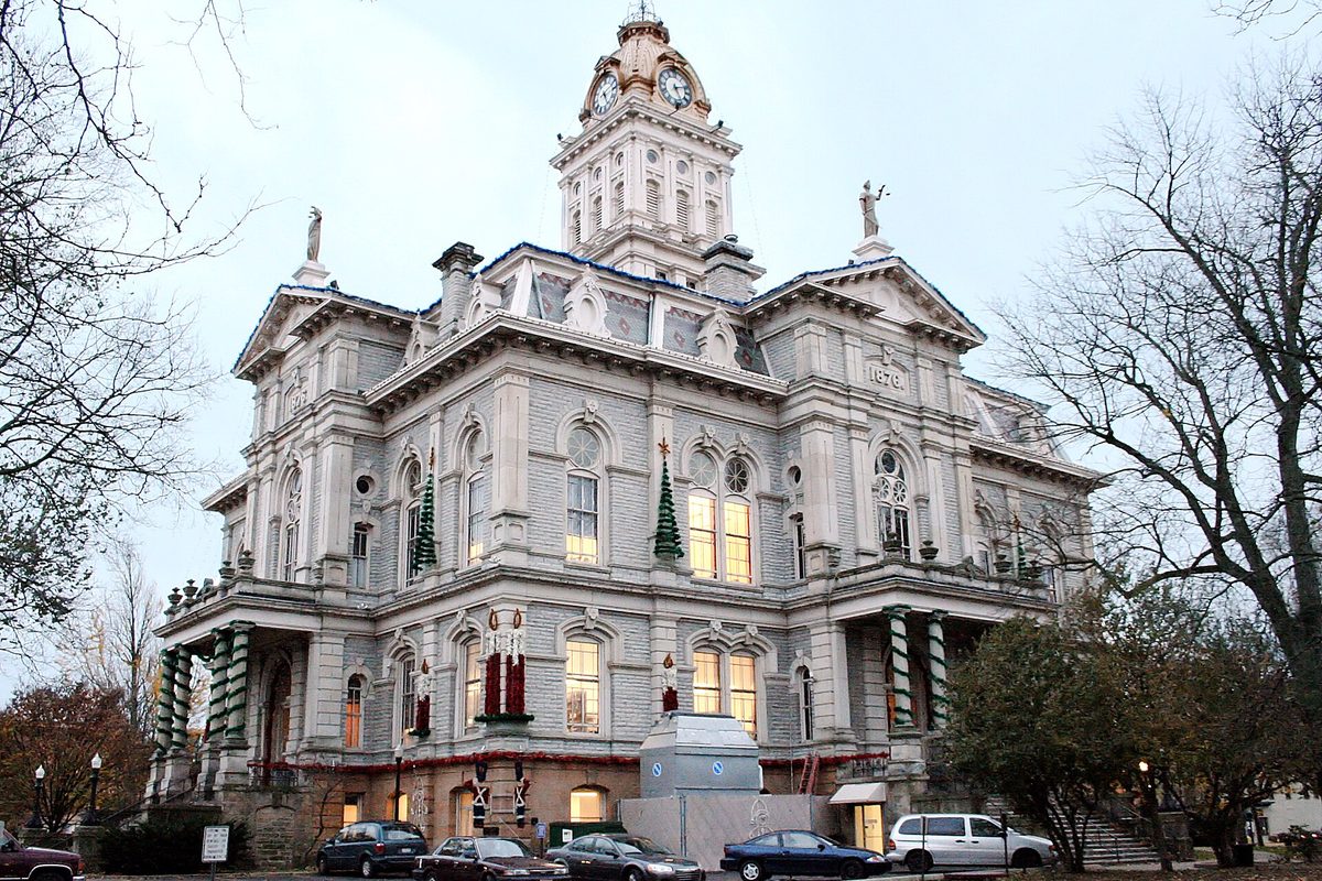 The gray stone courthouse in Newark at dusk, with a clock tower, lit windows, holiday garlands on the columns and cars parked along the street