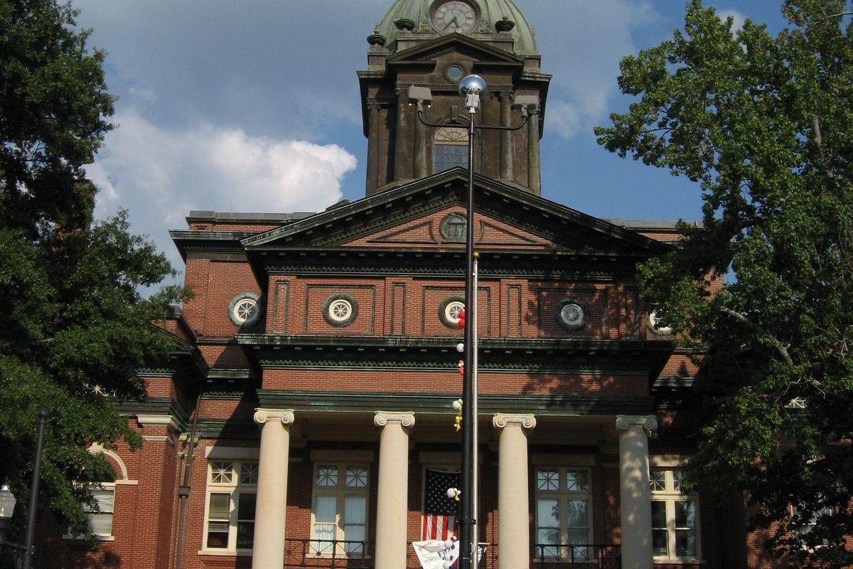 The red brick Coweta County Courthouse in Newnan, with a columned portico, round windows and a green domed clock tower, framed by trees