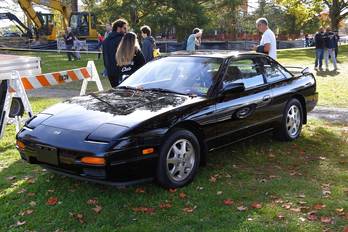 A black 1993 Nissan 240SX SE with its pop-up headlights closed, parked on the grass at an outdoor car show