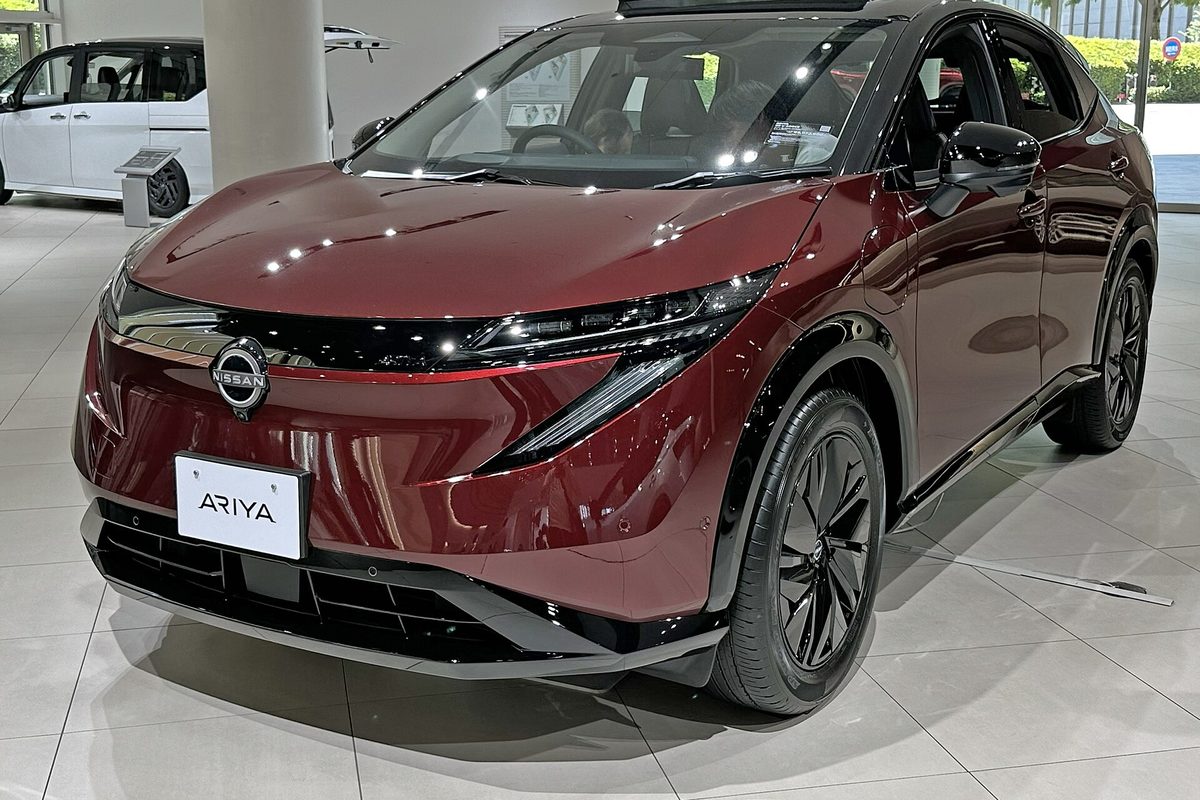 A dark red Japanese-market Nissan Ariya e-4ORCE on a white tiled showroom floor