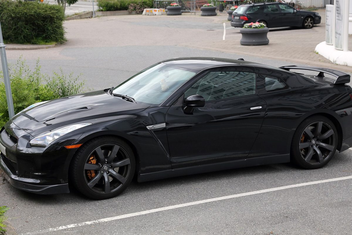 A black 2009 Nissan GT-R R35 coupe with dark wheels parked in a marked space beside a planter-lined lot