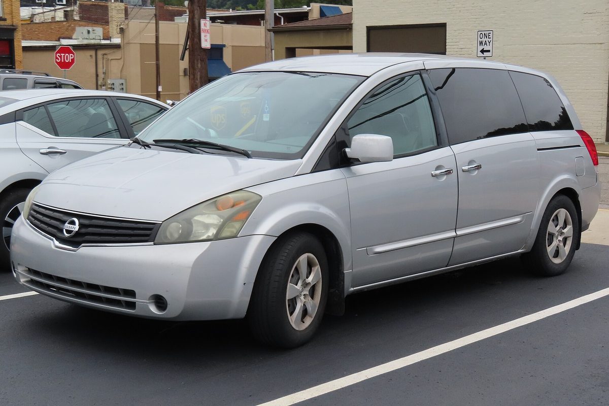 A silver 2007 Nissan Quest minivan in a parking lot, with a stop sign and a one-way sign behind it
