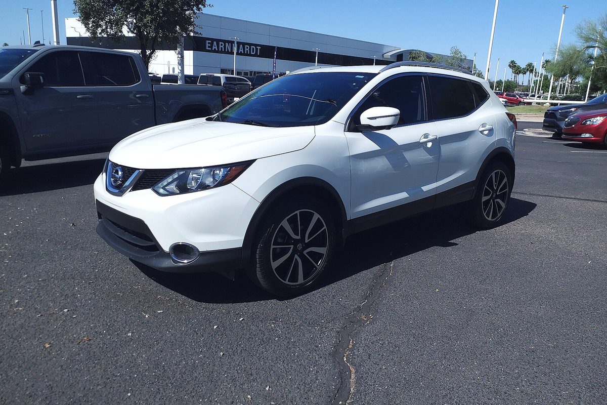 A white 2017 Nissan Rogue Sport SL parked on a dealership's asphalt lot under a clear blue sky