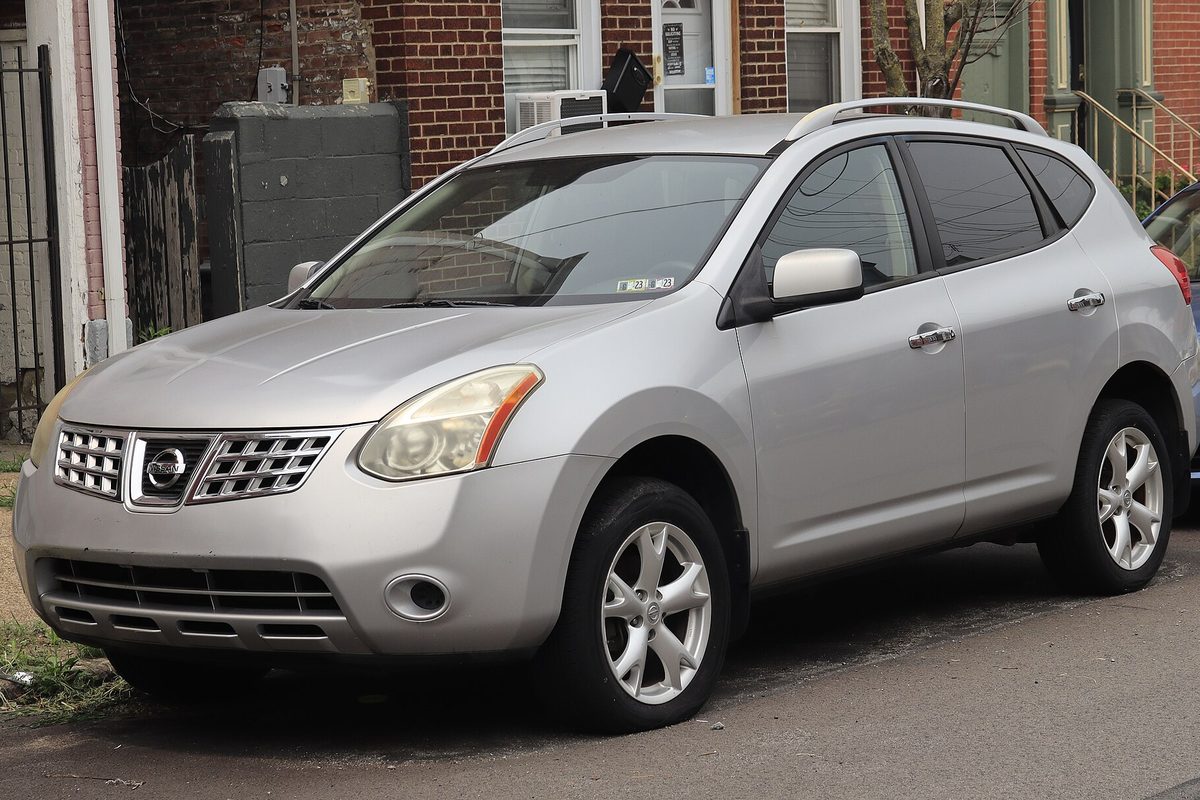 A silver 2010 Nissan Rogue SL parked at a curb in front of brick row houses