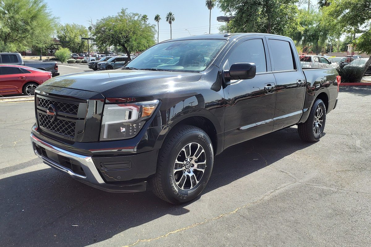 A black 2021 Nissan Titan SV crew cab pickup parked on a sunny lot, with palm trees and other cars behind it