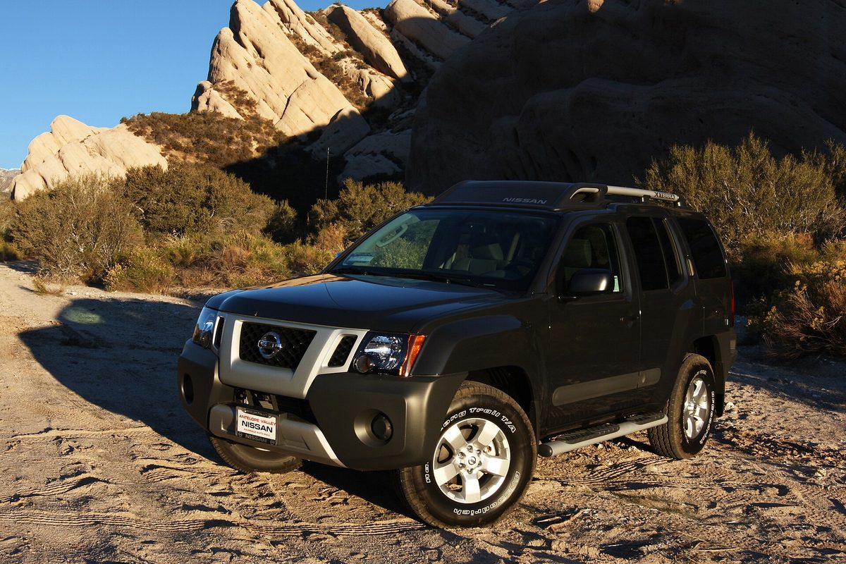 A dark gray 2011 Nissan Xterra S 4x4 parked on a sandy dirt trail below tall sandstone rocks