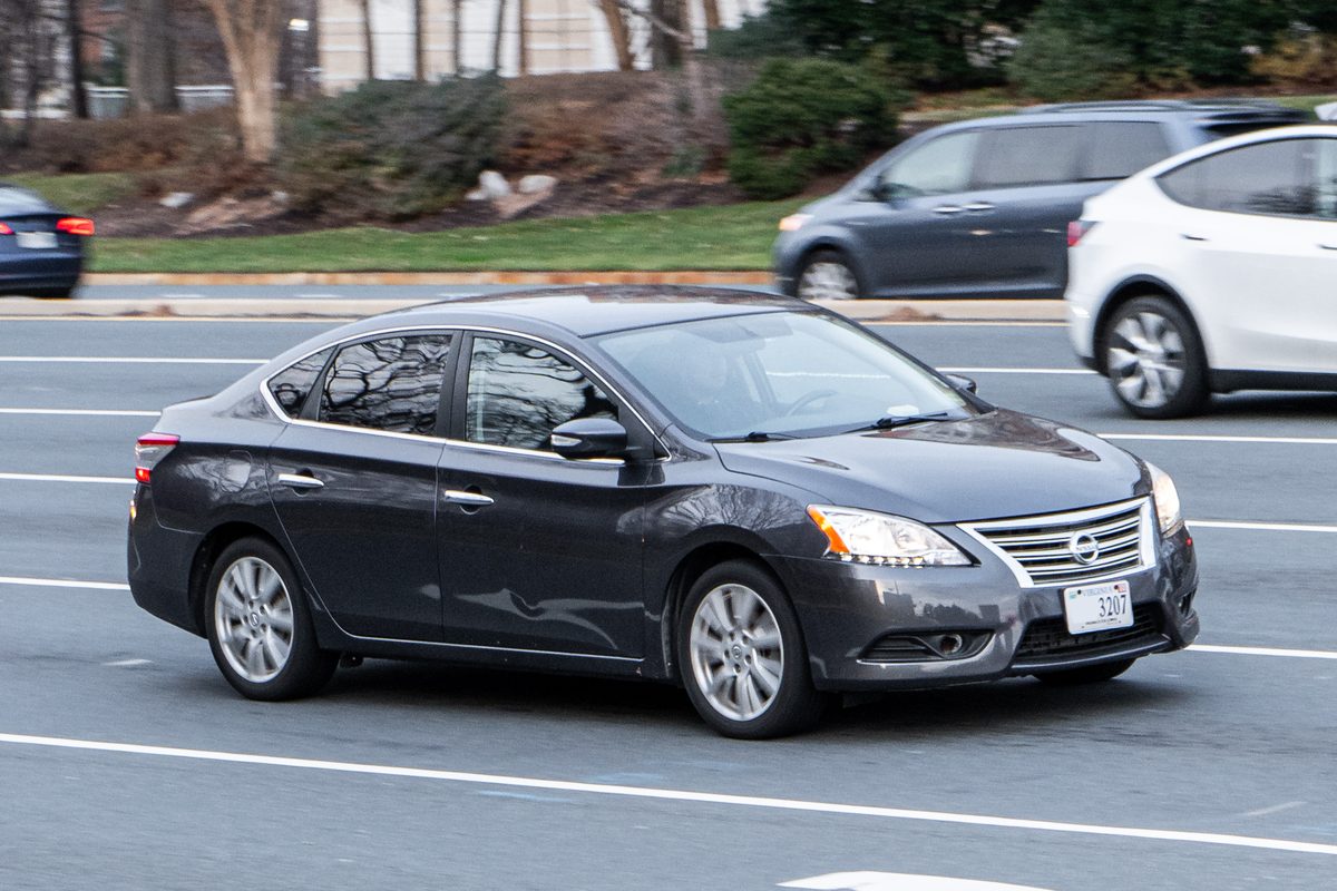 A dark gray Nissan Sentra sedan of the 2013-2019 generation driving on a multi-lane road in the Washington, D.C., area