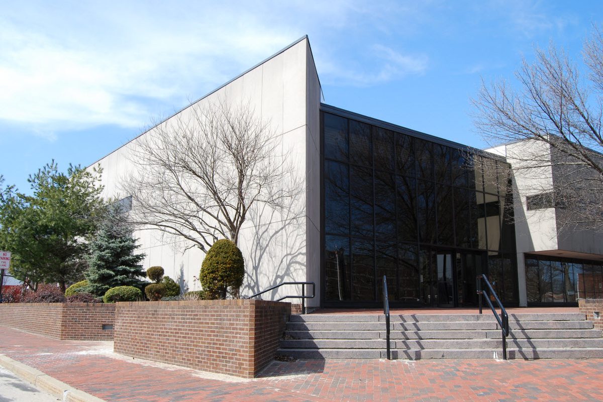North Attleborough Town Hall, a pale concrete building with a wall of dark glass, brick planters and wide granite steps under a blue sky