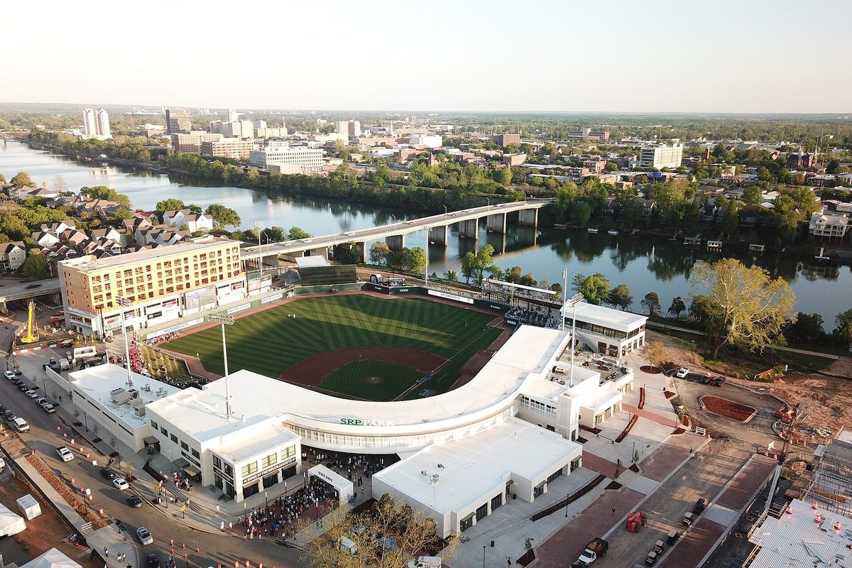 Aerial view of SRP Park, North Augusta's ballpark, beside a river with a long bridge and a city skyline beyond