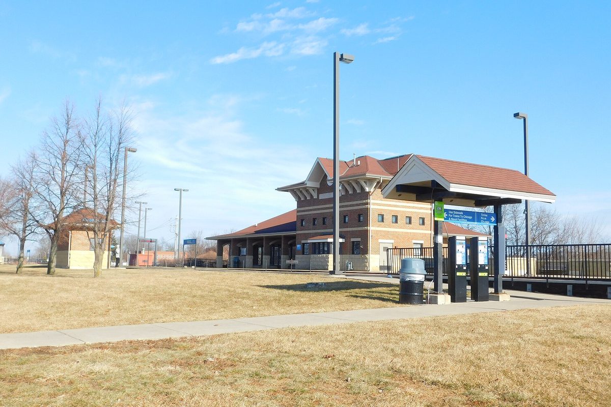 The Great Lakes Metra station in North Chicago, a brick building with red tile roofs, beside a covered platform and dry winter grass