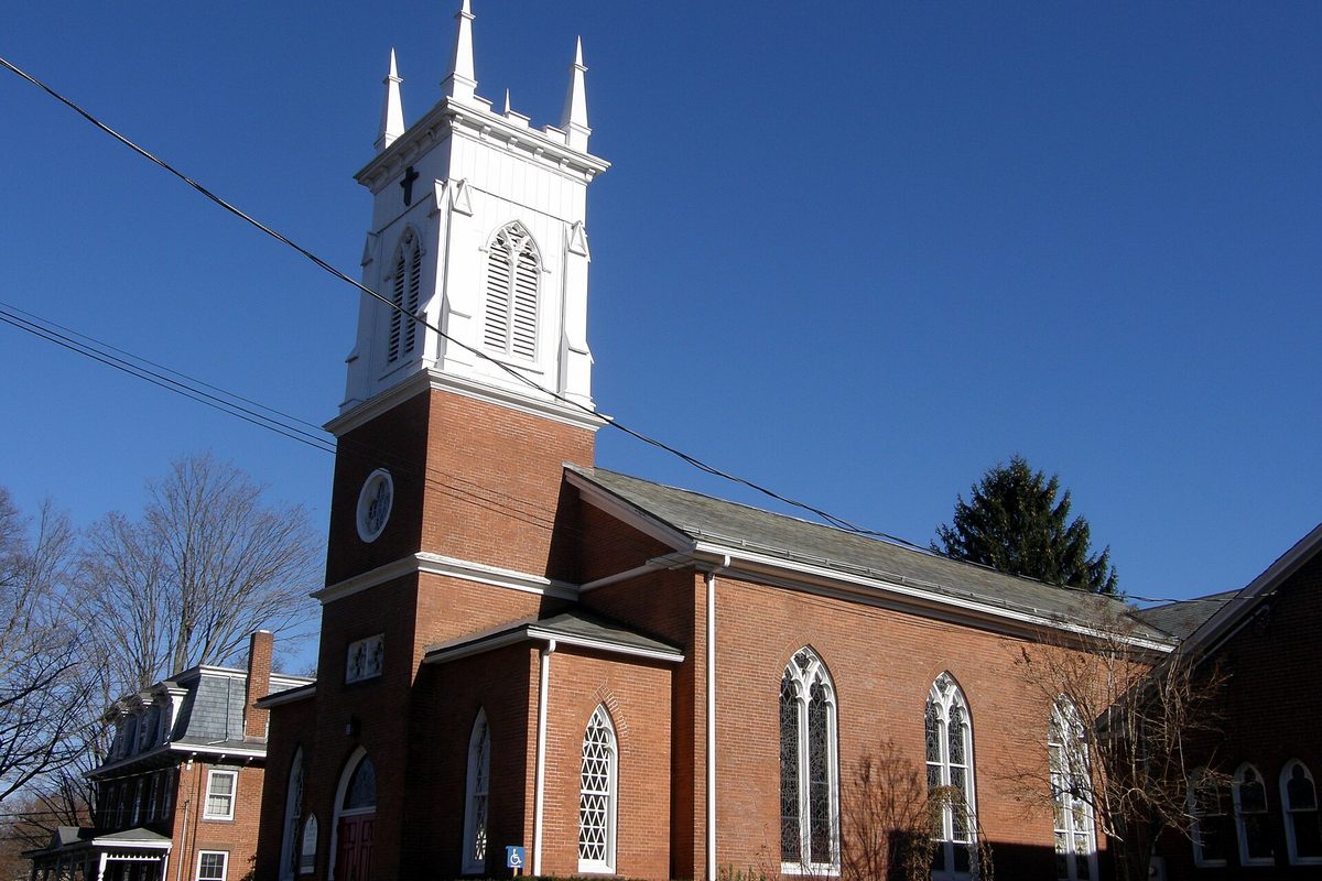 St. John's Episcopal Church in North Haven, a red brick church with a white steeple and tall pointed windows, under a deep blue sky beside bare trees