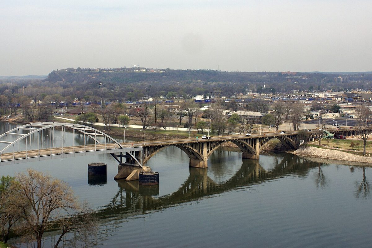 Arched bridges crossing the Arkansas River toward North Little Rock, with low wooded hills and buildings on the far bank