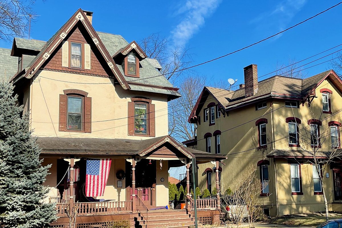 Two Victorian houses on Washington Avenue in North Plainfield, one with an American flag hanging from its front porch, under a clear blue sky