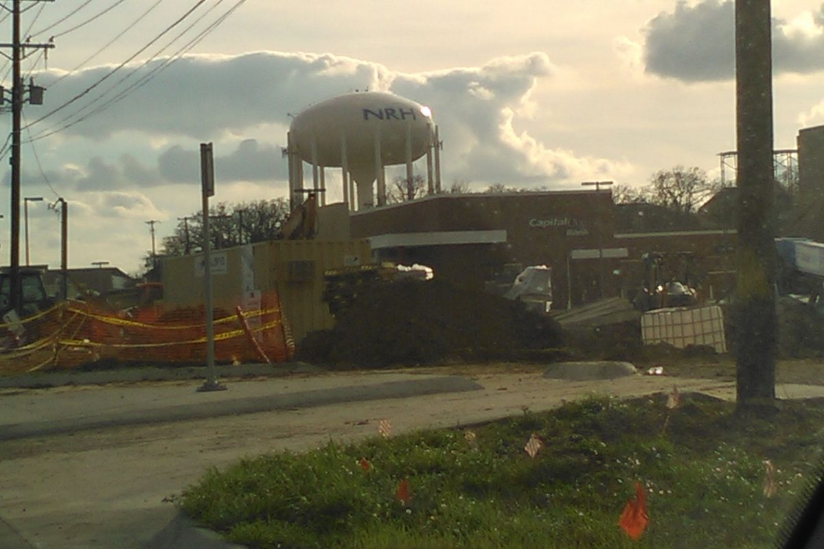 The white North Richland Hills water tower marked NRH, seen over a construction site with orange fencing on Davis Boulevard