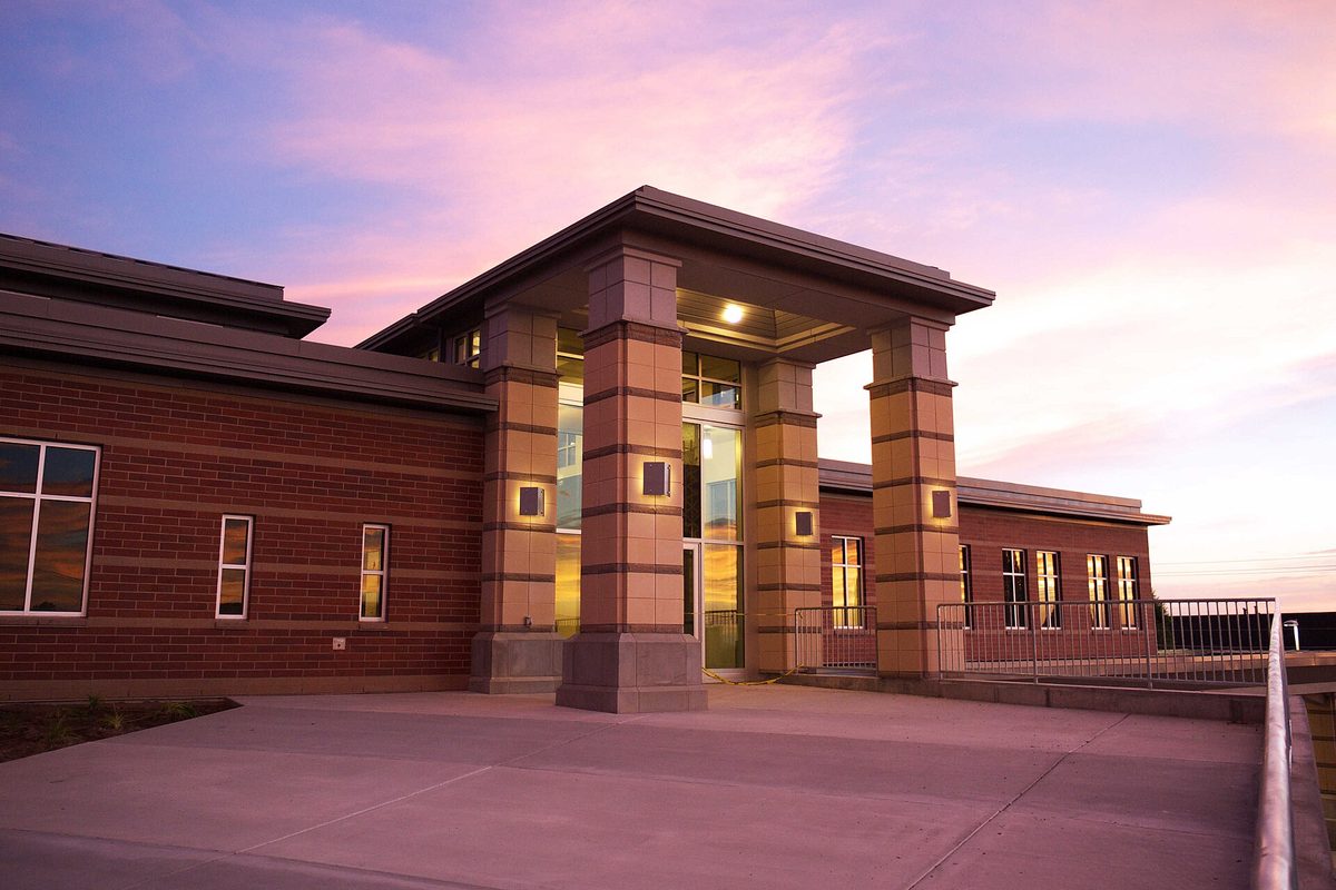 The lit entrance of North Salt Lake City Hall, square stone pillars against a brick building under a pink and purple sunset sky