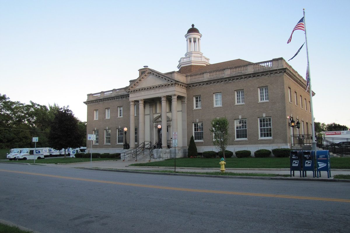 North Tonawanda's 1912-1914 post office, a stone building with columns and a white cupola, with mail trucks parked beside it and blue mailboxes at the curb
