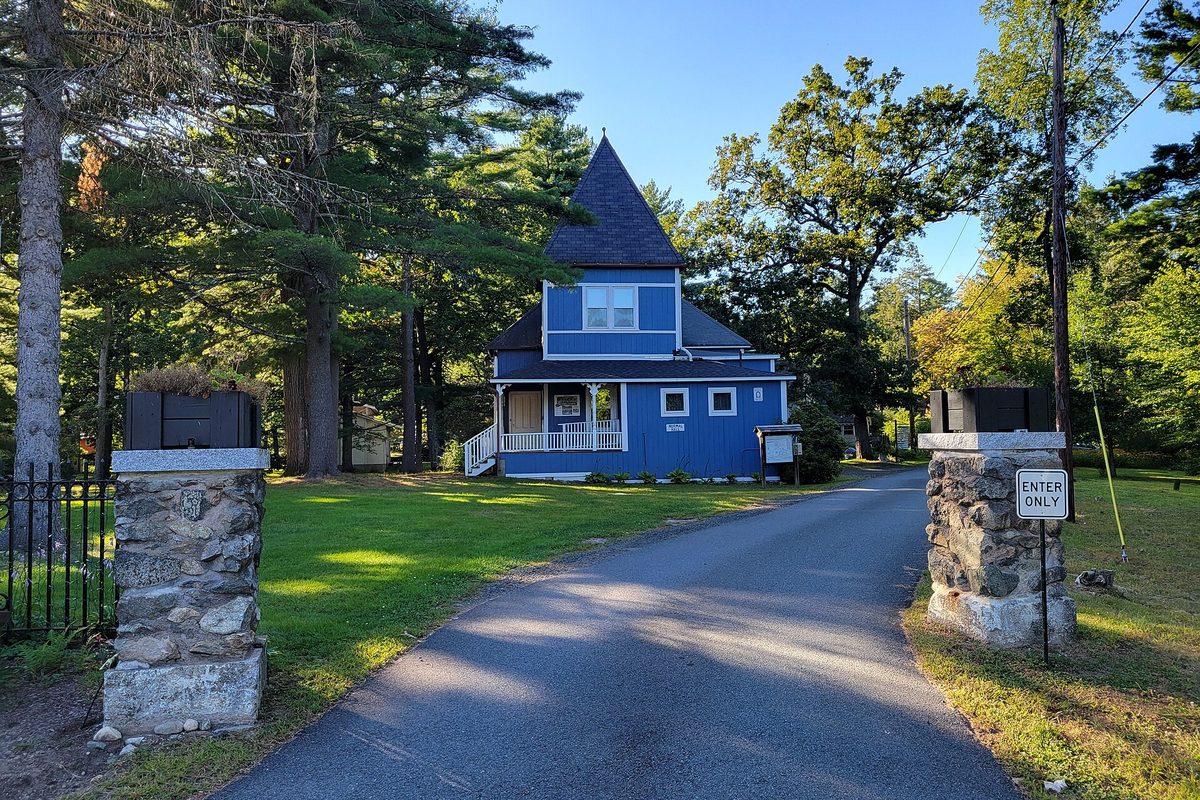 A blue Victorian house with a pointed tower roof behind two stone gate pillars and an Enter Only sign on the drive into Laurel Park, Northampton