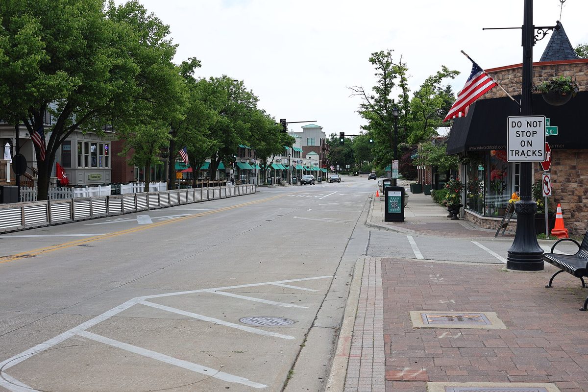 Downtown Northbrook looking down Shermer Road, with shops, street trees, an American flag and a Do Not Stop on Tracks sign by the sidewalk