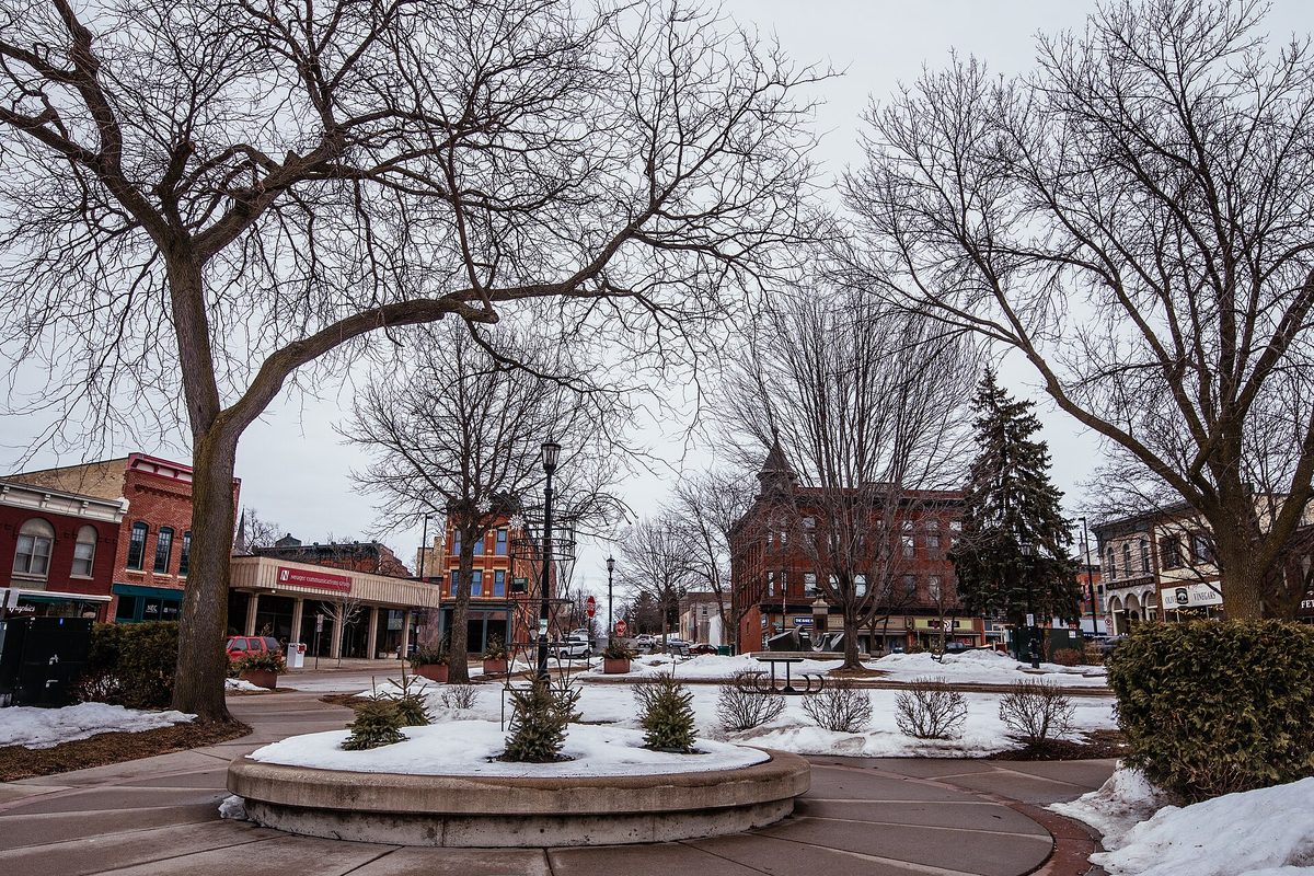Bridge Square in downtown Northfield in winter, with bare trees, snow on the ground and brick storefronts behind a round planter