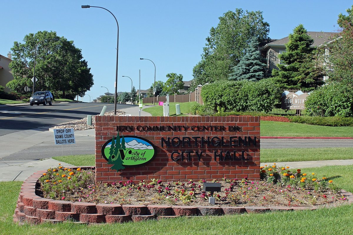 A brick sign reading Northglenn City Hall, 11701 Community Center Drive, with a bed of orange and pink flowers in front and homes and trees behind