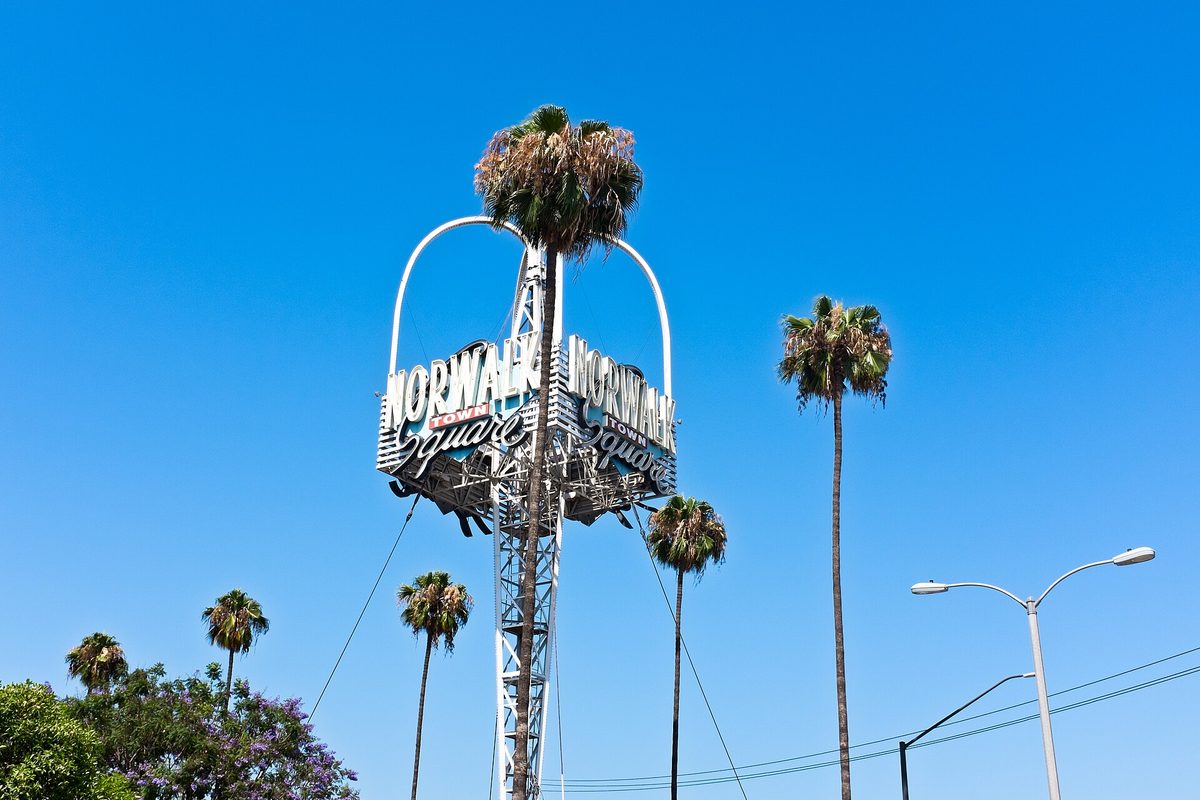 The tall Norwalk Town Square sign on a steel lattice tower among palm trees against a clear blue sky