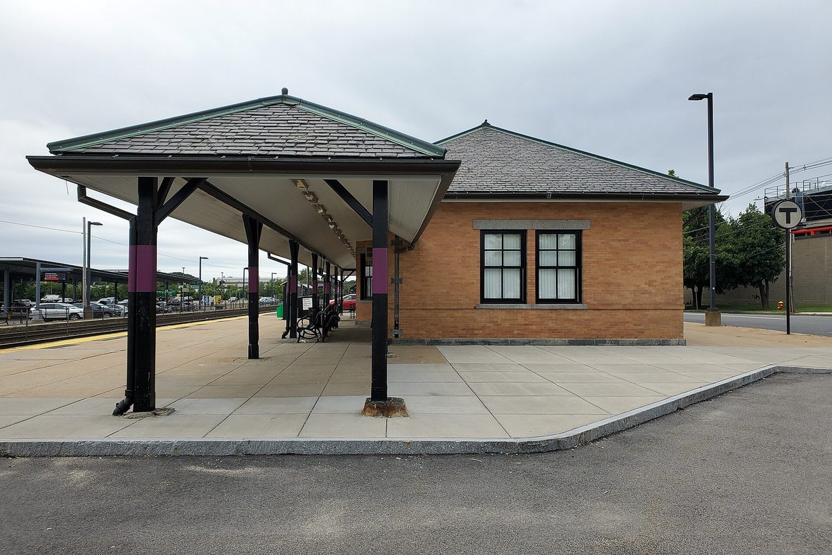 The former Norwood Central station building, a tan brick depot with a hip roof and a long covered platform on dark posts, under a cloudy sky
