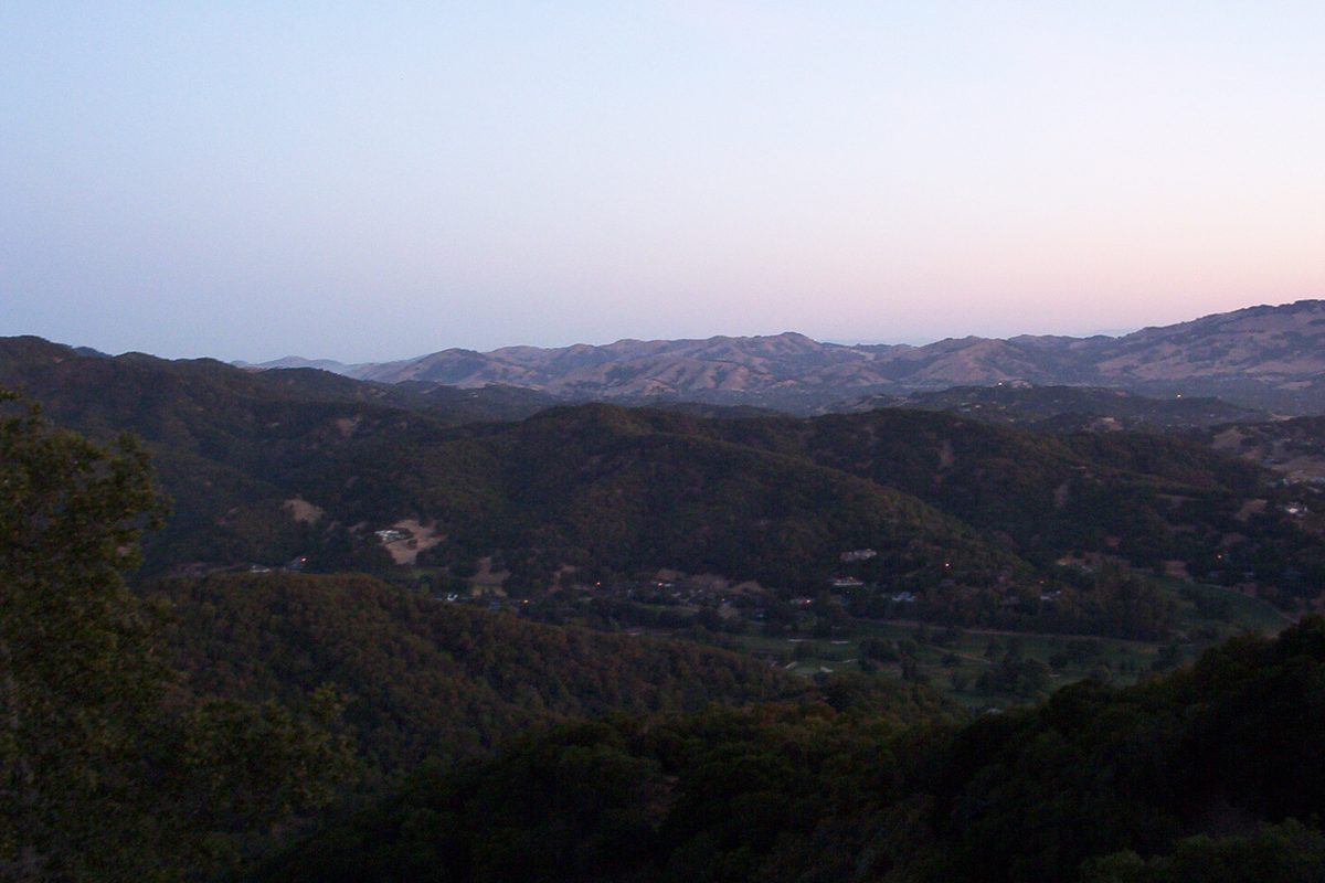 Wooded ridges and grassy hills outside Novato at dusk, seen from a hiking trail under a pale pink sky