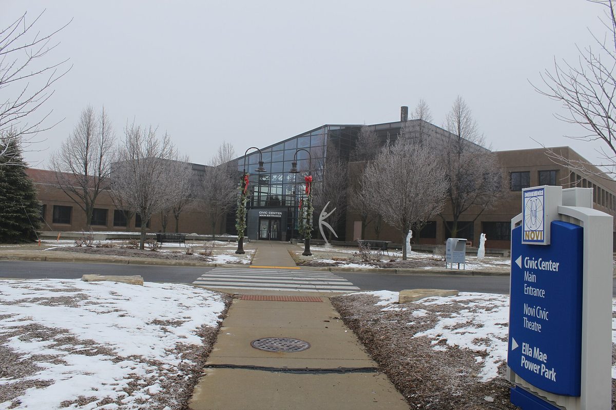The Novi Civic Center entrance in winter, with a blue sign pointing to the Civic Center, Civic Theatre and Ella Mae Power Park and snow on the lawns