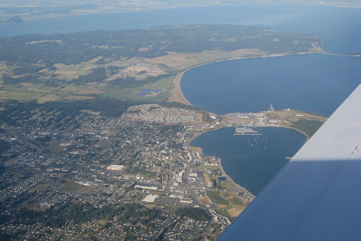 Aerial view from a small plane of Oak Harbor on Whidbey Island, with the town's streets, a marina and a curving bay, and the plane's wing in the corner