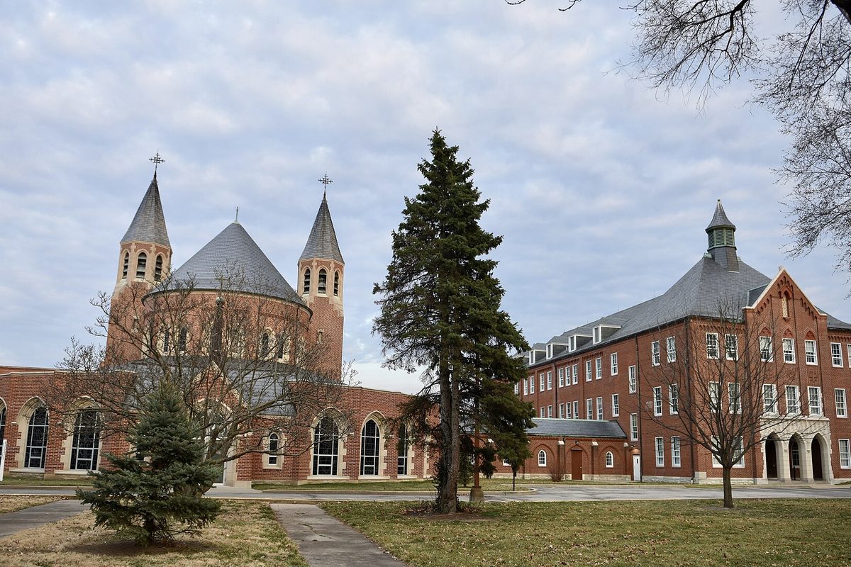 St. Mary's Institute in O'Fallon: red brick buildings with conical towers and a tall evergreen on the lawn under a cloudy sky