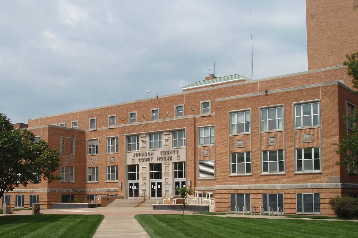 The red brick Johnson County Courthouse in Olathe, a four-story building with its name over the entrance, a lawn and a walkway in front