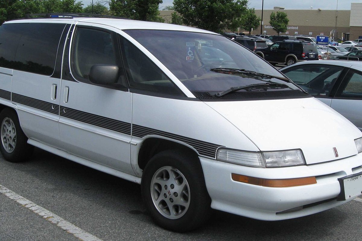 A white first-generation Oldsmobile Silhouette minivan with a dark lower stripe, parked in a store lot