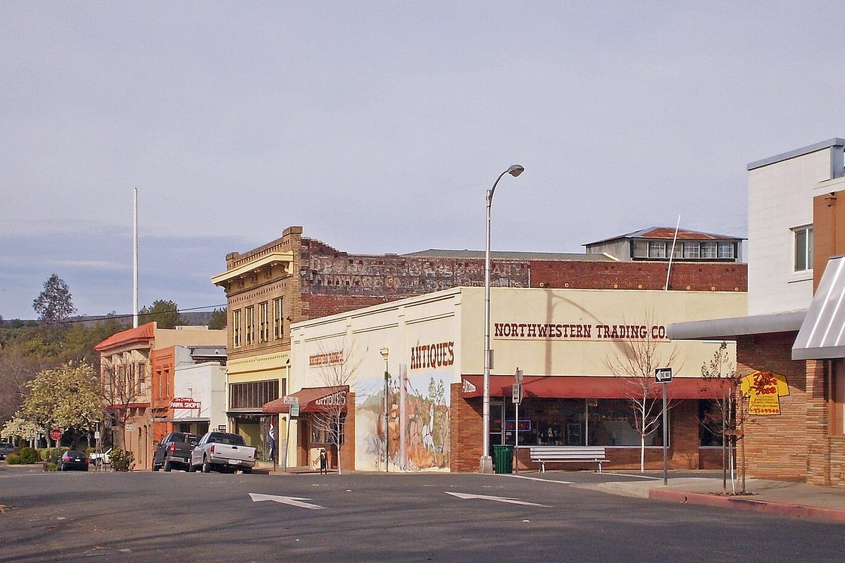 Historic downtown Oroville: brick storefronts including an antiques shop with a painted mural and the Northwestern Trading Co., with pickups parked at the curb