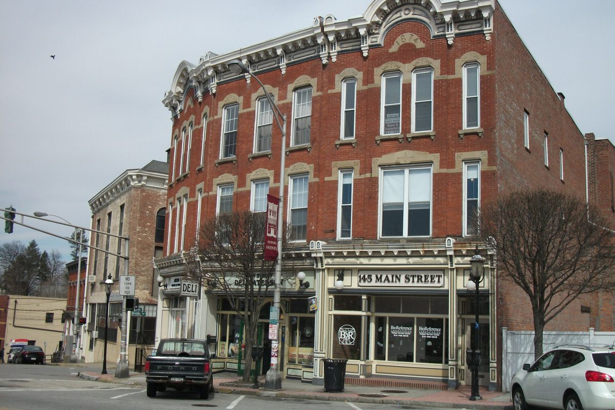 A three-story red brick building with ornate cream trim at 145 Main Street in Ossining, with shops on the ground floor and a pickup truck parked out front