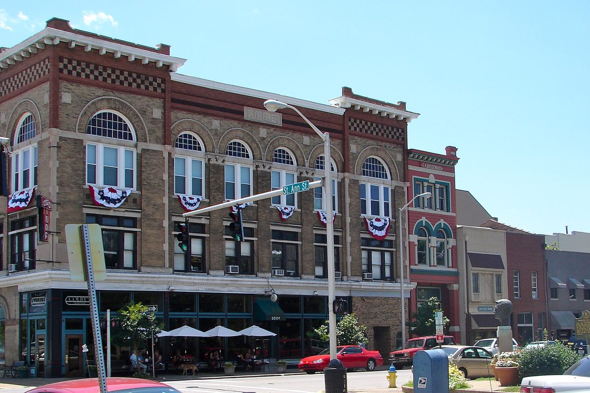 A brick and stone corner building at West 3rd and St. Ann Streets in downtown Owensboro, with red, white and blue bunting under its arched windows and a red car parked out front