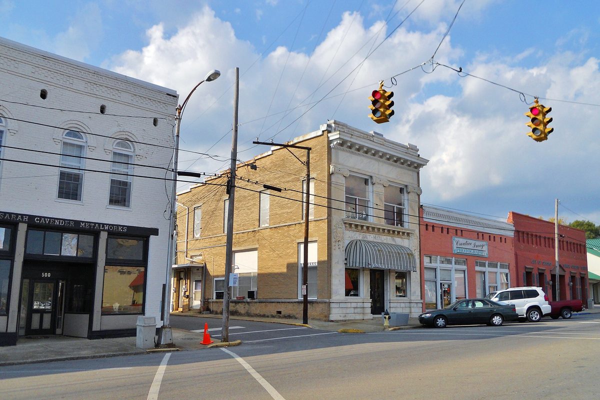 A downtown Oxford street corner with a white two-story storefront, a tan brick building with a carved cornice and traffic lights hanging over the intersection