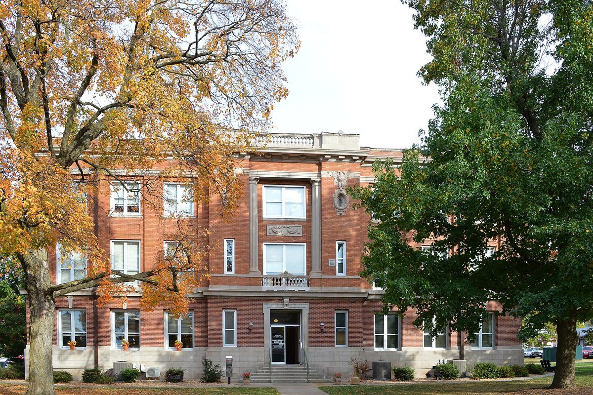 The historic red brick Christian County Courthouse in Ozark, with a stone balustrade on the roof, framed by autumn trees