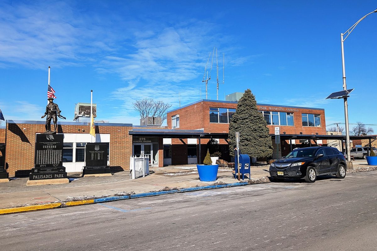 The red brick Palisades Park municipal complex on Broad Avenue, with a veterans' monument and soldier statue out front under a clear blue sky