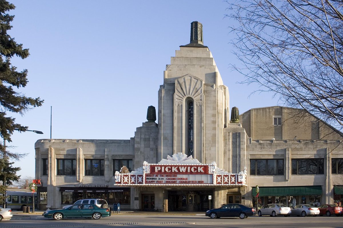 The art deco Pickwick Theatre and its red marquee in downtown Park Ridge, with cars parked along the street under a clear blue sky