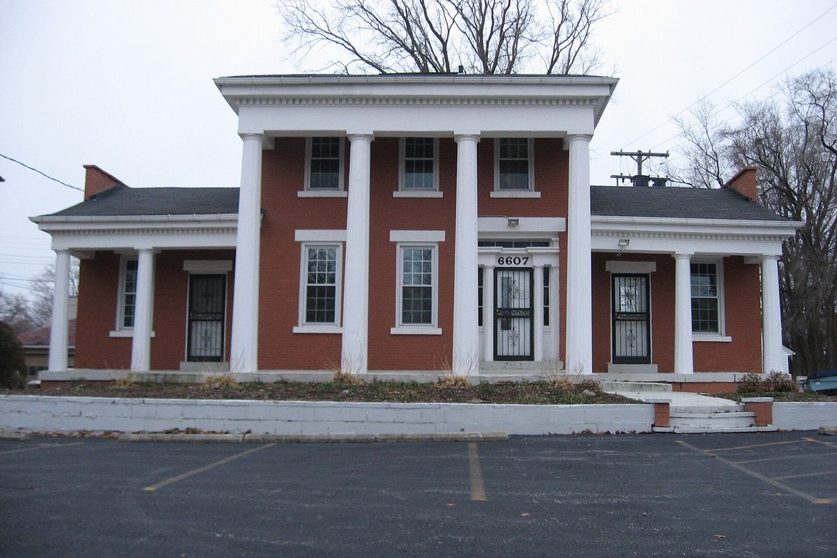 The Robert W. Henry House on Pearl Road in Parma Heights, a red-brick house with tall white columns and the number 6607 over the door, behind an empty parking lot