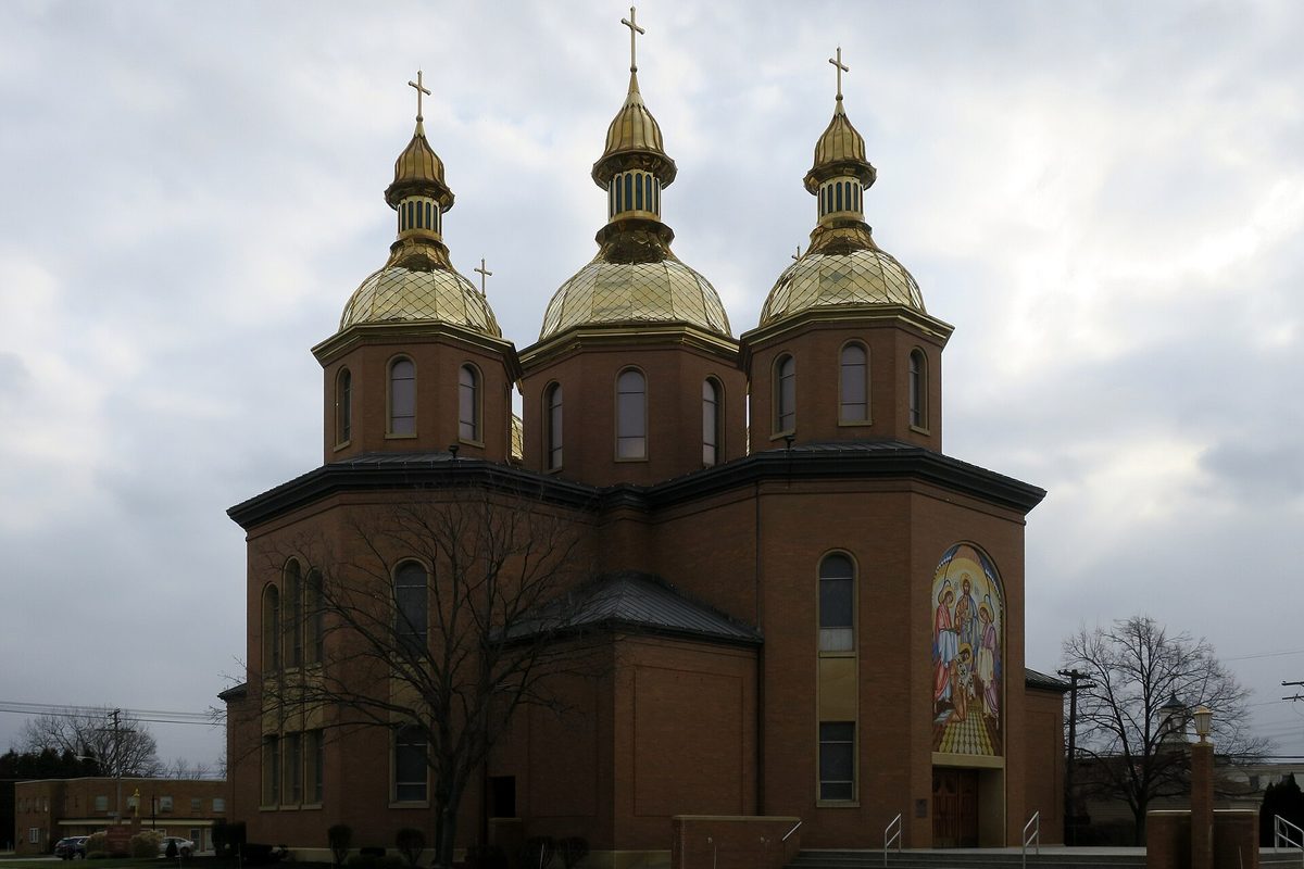 St. Josaphat Ukrainian Catholic Cathedral in Parma, a brick church with three gold domes and a tall mosaic of saints, under a gray sky
