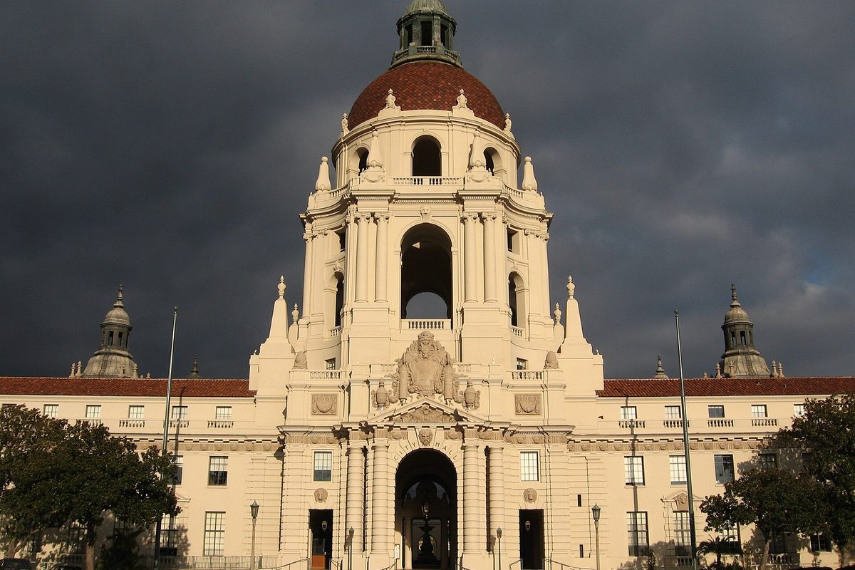 The domed tower of Pasadena City Hall lit by low sun against dark storm clouds, with trees on either side