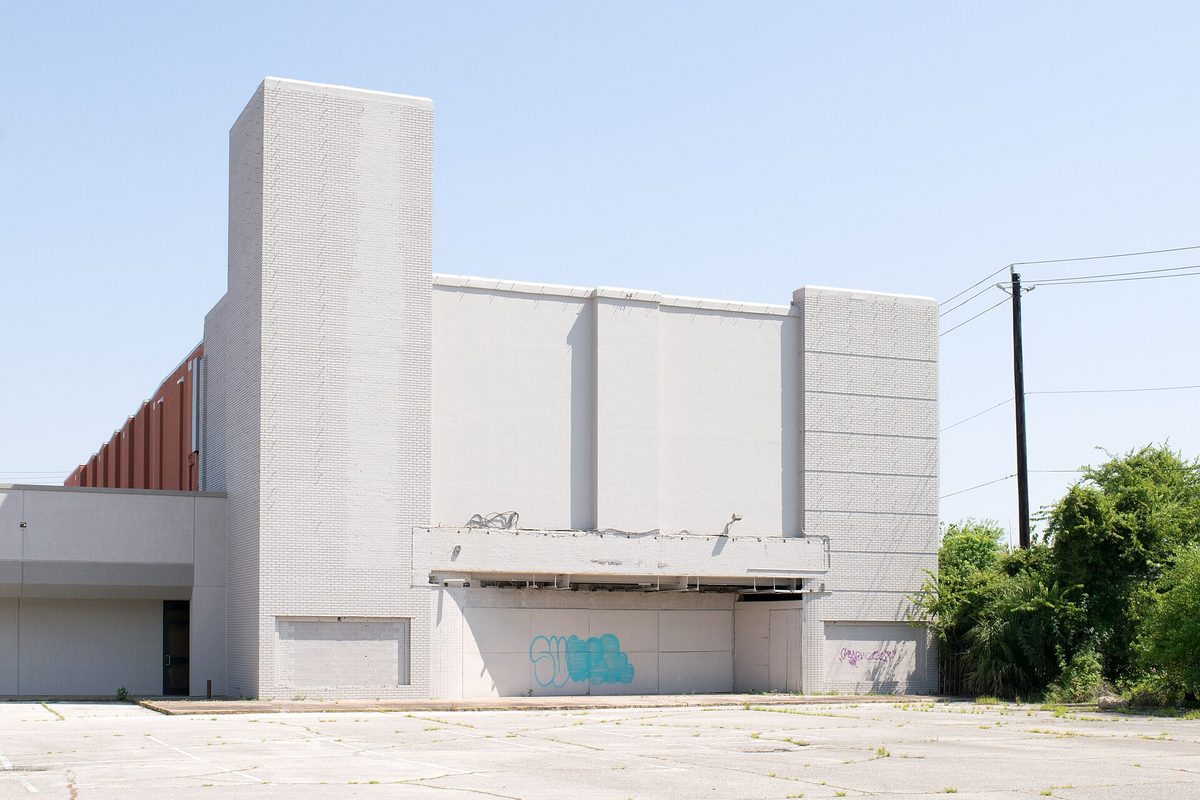 The shuttered former Capitan Theater in Pasadena, Texas, a pale gray windowless building with graffiti under its empty marquee, facing a cracked and weedy parking lot
