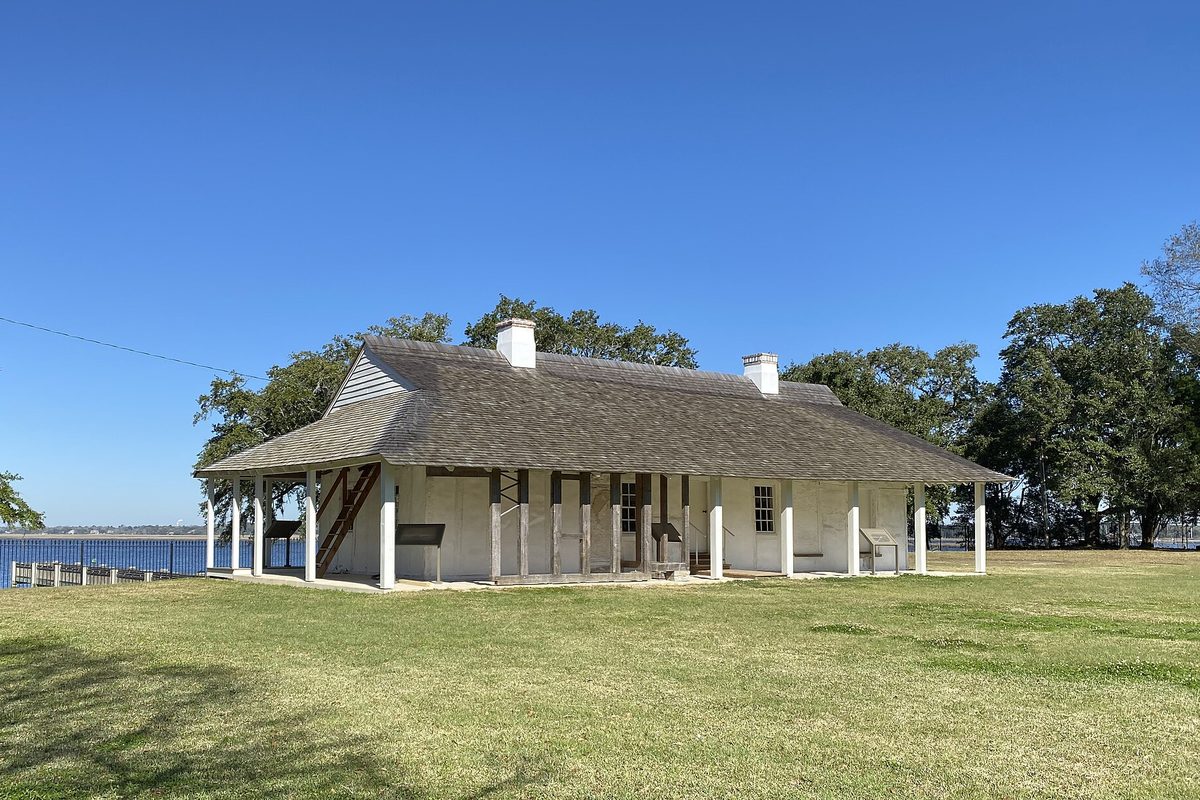The low white LaPointe-Krebs House with its broad shingled roof on a green lawn beside the water in Pascagoula