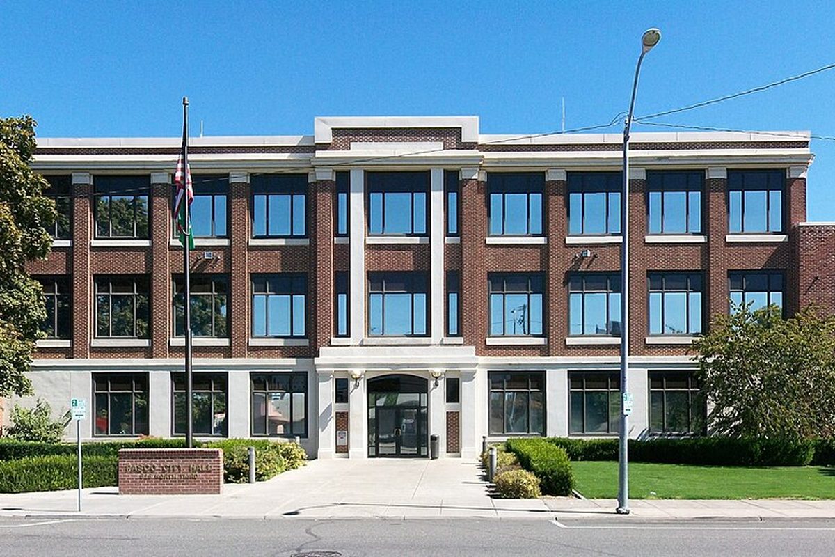 Pasco City Hall, a three-story brick building with white trim, a flagpole and a low brick sign out front, under a blue sky