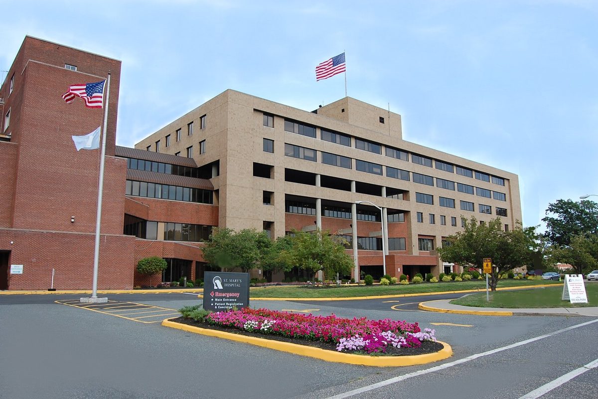 The main building of St. Mary's Hospital on Boulevard in Passaic, a tan and brick tower with flags out front and a pink flower bed by the entrance drive
