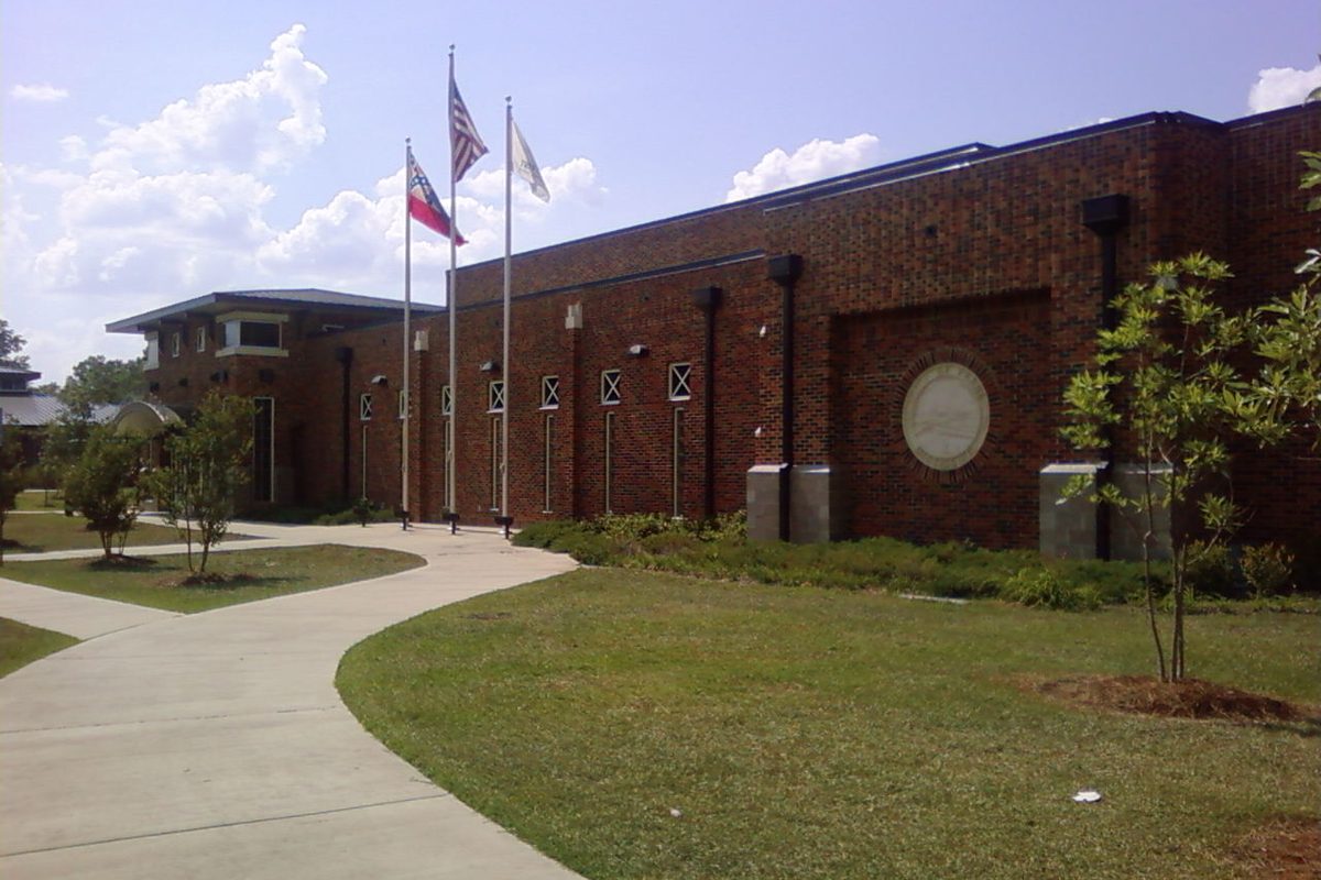 The red brick Pearl Community Center with three flagpoles and a curving sidewalk across a green lawn