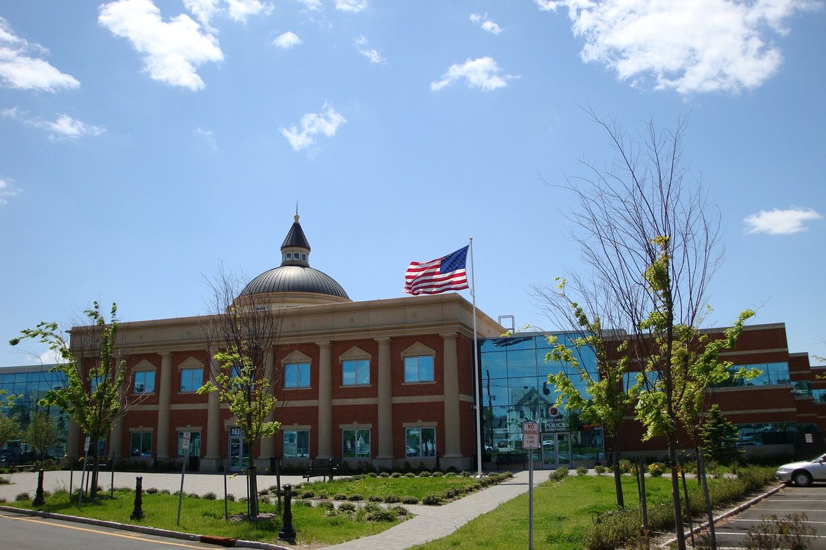 Perth Amboy's courthouse and police headquarters, a red brick building with white columns and a silver dome beside a glass wing, with an American flag out front